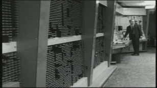 "Black-and-white photograph of the TX-2 memory-bank hardware at MIT Lincoln Laboratory: rows of cabinet frames, wiring bundles, and indicator hardware typical of late-1950s machines. The image grounds the historical discussion of early partitioned arithmetic in real physical equipment."